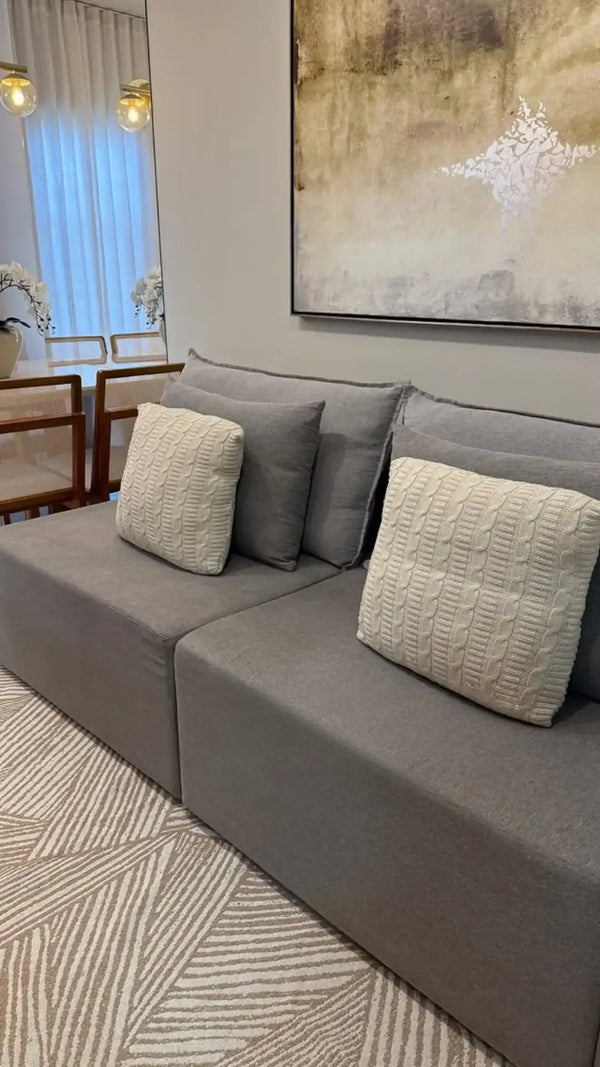 Sofá sectional cinza com almofadas texturizadas creme e tapete moderno com padrão geométrico.