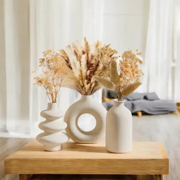 Vaso de cerâmica branca com pescoço torcido e flores secas dentro.